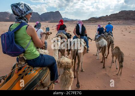 Les touristes ont partir en fin d'après-midi pour une promenade à dos de chameau à travers Wadi Rum (vallée de la Lune). Wadi Rum est une vallée naturellement coupée en roche. Banque D'Images