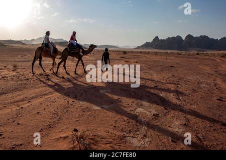 Les touristes ont partir en fin d'après-midi pour une promenade à dos de chameau à travers Wadi Rum (vallée de la Lune). Wadi Rum est une vallée naturellement coupée en roche. Banque D'Images
