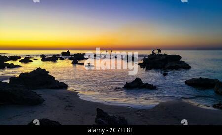 silhouettes de pêcheurs qui jettent des tiges sur une plage rocheuse au coucher du soleil Banque D'Images