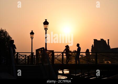 Silhouettes de personnes méconnaissables sur le pont au-dessus de la Seine devant la lumière du coucher du soleil. Lanterne vintage, lumières de rue sur fond de couleur orange Banque D'Images