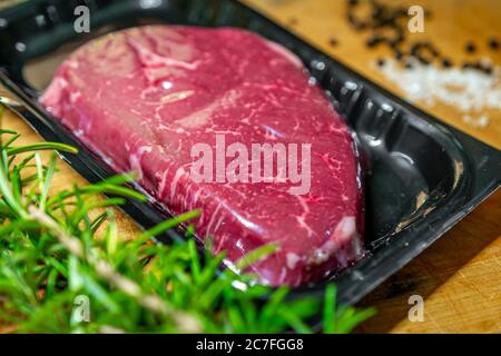 Steak de bœuf dans un emballage sous vide et épices sur planche à découper en bois Banque D'Images