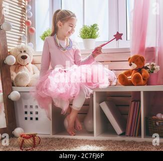 Une fille heureuse joue avec une baguette magique et un ours en peluche à la maison. Drôle, un enfant adorable s'amuse dans la chambre des enfants. Banque D'Images