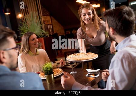 Jolie femme de serveur servant des groupes d'amis avec de la nourriture dans le restaurant Banque D'Images