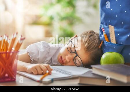Retour à l'école! Joyeux mignon enfant industriel est assis à un bureau à l'intérieur. Enfant apprend en classe. La fille est fatiguée et dort. Banque D'Images