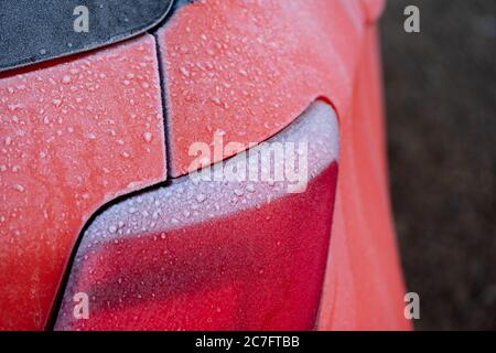 Gros plan, faible concentration de cristaux de glace vus à l'arrière d'un témoin lumineux d'une voiture japonaise vue dans une salle d'exposition extérieure en milieu d'hiver. Banque D'Images