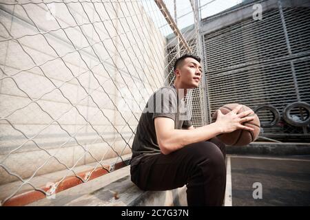 asiatique jeune adulte joueur de basket-ball assis au bord de la cour Banque D'Images