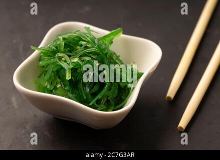 Sélection sélective, salade de Chuka de mer aux graines de sésame dans des plats en céramique blanche, avec des bâtonnets de bambou sur fond sombre Banque D'Images