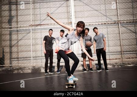 jeune femme asiatique skateboarder skate en plein air avec des amis regardant de derrière Banque D'Images