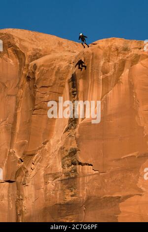 USA, Utah, Moab, UN cavalier de base s'envoler du sommet de la face verticale de 400 pieds de la tombe dans le canyon de Kane Springs. Observez son ombre sur la falaise. Banque D'Images