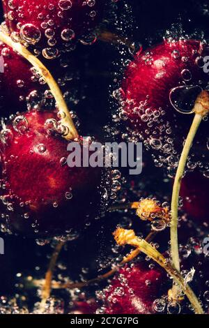 De délicieuses cerises douces avec bulles dans l'eau sur fond sombre de près. Boisson gazeuse à la cerise Banque D'Images