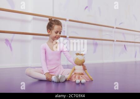 Adorable petite ballerine s'étirant avant de pratiquer le ballet à l'école de danse, assis à côté de sa poupée, espace de copie Banque D'Images