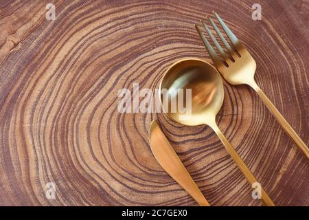 Le couteau doré, la fourchette et la cuillère se trouvent sur une tranche d'arbre. table en bois. Avec espace de copie. Banque D'Images