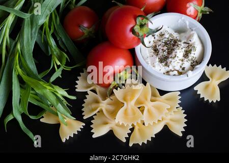 Spaghetti et farfale ingrédients tomates et soute avec des épices sur le fond noir, studio de tir. Banque D'Images