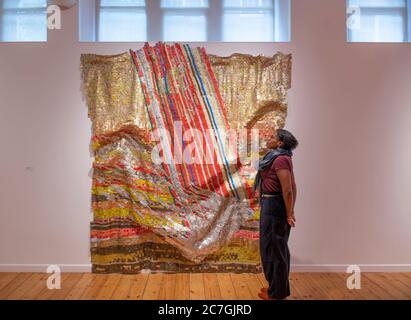 Londres, Royaume-Uni. 17 juillet 2020. Focus sur l'exposition El Anatsui à la Galerie d'octobre se déroule du 15 juillet au 8 août 2020 et présente des œuvres métalliques et une sélection de tirages créés en association avec le Factum Arte, Madrid. El Anatsui est aujourd'hui mieux connu pour ses travaux composés de plusieurs milliers de bottle-tops en aluminium. Le directeur de la galerie Saara étudie le changement d'installation dans Fortune, 2018, aluminium et cuivre. Crédit: Malcolm Park/Alay Live News. Banque D'Images