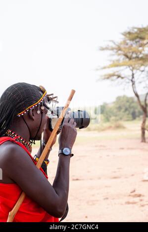 Homme de Maasai souriant portant une tenue traditionnelle, prenant des photos. Réserve nationale de Maasai Mara. Kenya. Afrique. Banque D'Images