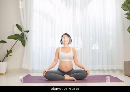 Femme enceinte faisant du yoga dans la salle de séjour, concept sain et soins. Banque D'Images
