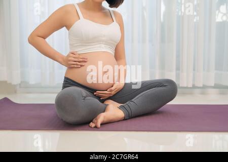 grossesse, personnes et maternité concept - heureuse femme enceinte asiatique appliquant la crème de marque extensible au ventre Banque D'Images