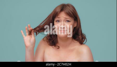 Une femme caucasienne malheureuse tient des extrémités de cheveux regardant la caméra. Triste belle dame a besoin de soins de cheveux ayant un problème avec sa coiffure. Isolé sur la couleur Banque D'Images