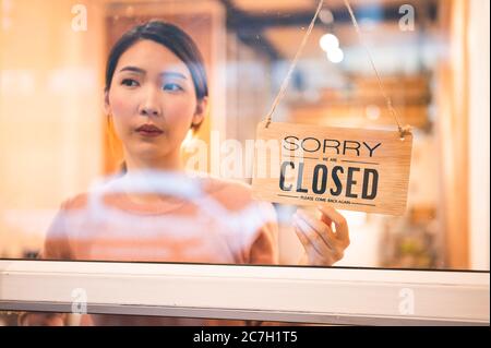 Femme asiatique propriétaire de magasin tournant pendante panneau fermé dans la porte avant de son magasin Banque D'Images