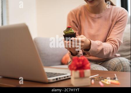 Femme asiatique célébrant son anniversaire par vidéoconférence en ligne, à la maison, tout en restant isolée à la maison. Main tenant un gâteau de tasse Banque D'Images