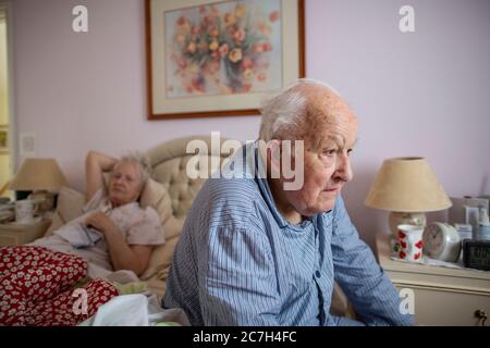 Un couple âgé dans les années 80 s'est assis sur le lit dans son pyjama avant de se lever dans le matin, Angleterre, Royaume-Uni Banque D'Images