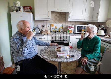 Un couple âgé dans les années 80 prenant des médicaments tout en étant assis à la table du petit déjeuner buvant une tasse de thé le matin, Angleterre, Royaume-Uni Banque D'Images