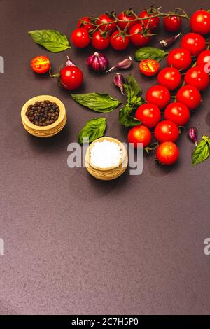 Concept de cuisine. Tomates cerises mûres, ail, basilic, sel et grains de poivre noir. Arrière-plan en béton noir et en pierre, espace de copie Banque D'Images
