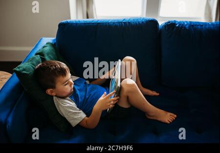 Vue de dessus de la tête d'un jeune garçon allongé sur un canapé avec tablette Banque D'Images