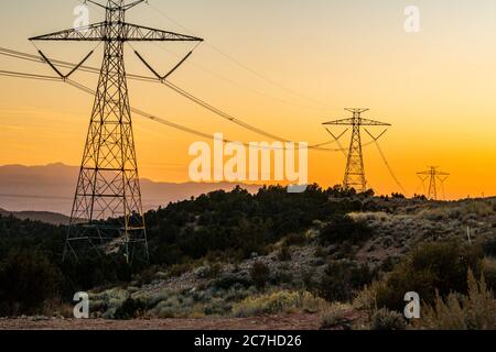 Vue sur les poteaux électriques haute puissance sur les collines vertes pendant heure du coucher du soleil Banque D'Images