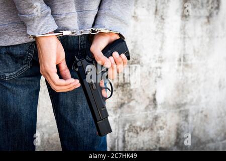 Fermez les mains attachées les menottes et tenez le pistolet derrière son corps. Homme arrêté menotté les mains au dos. Banque D'Images