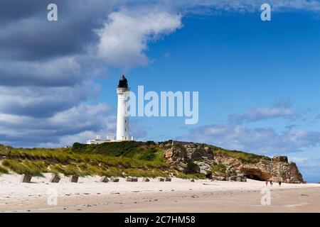 PLAGE DE LOSSIEMOUTH ET CÔTE DE MER MORAY ÉCOSSE EN ÉTÉ UN CIEL BLEU AVEC LE PHARE DE COVESEA ET LES RANDONNEURS RANDONNÉE SUR LA PLAGE Banque D'Images