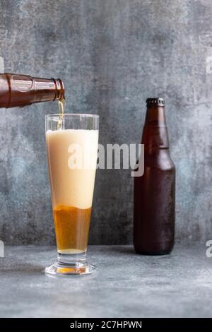 Verser la bière de la bouteille dans le verre sur le fond gris Banque D'Images