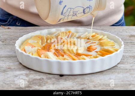 Préparez un gratin de pommes de terre, d'artichauts de citrouille et de Jérusalem, versez les ingrédients en tranches dans un moule beurré avec du lait et de la crème dans un pot Banque D'Images