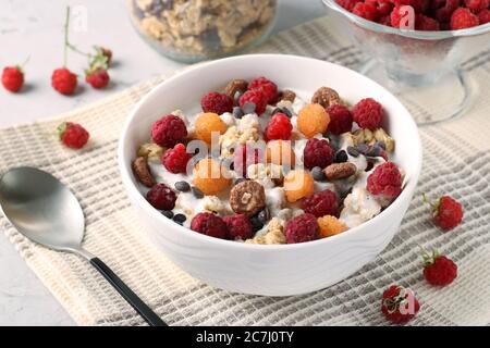 Muesli au miel croustillant de granola avec yaourt naturel, framboises rouges et jaunes fraîches, chocolat et noix dans un bol sur fond gris, aliments sains Banque D'Images