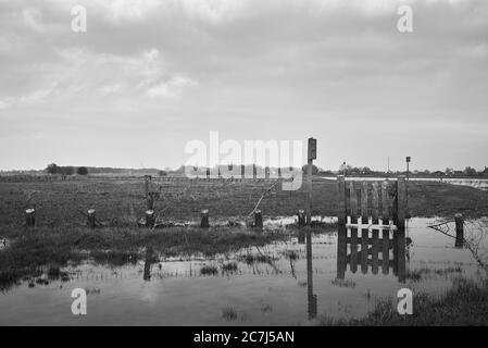 Photo en échelle de gris d'une petite clôture reflétée dans le lac dans une vallée dans une zone rurale Banque D'Images