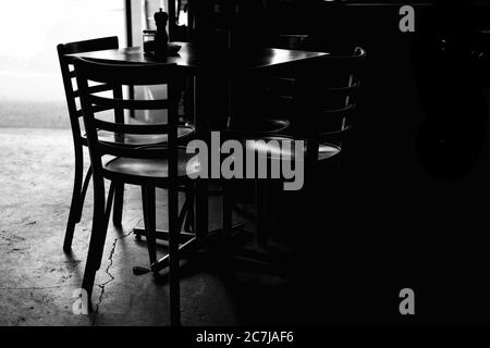 Prise de vue en niveaux de gris d'une table avec des chaises dans une obscurité chambre en journée Banque D'Images