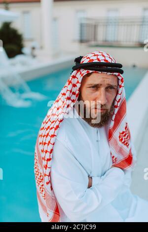 Portrait d'un beau musulman arabe du Moyen-Orient en vêtements traditionnels assis au bord de la piscine Banque D'Images
