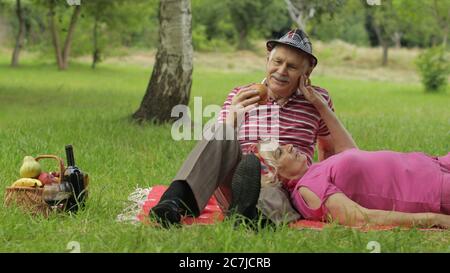 Pique-nique familial dans le parc. Les personnes âgées, les couples actifs de race blanche s'assoient sur une couverture et boivent du vin. Parler et célébrer l'anniversaire. Homme âgé, femme. Mari, femme. Grand-père, grand-mère Banque D'Images