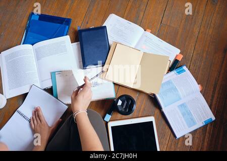 Gros plan photo de fille tenant le crayon à la main étudier avec une tablette, des livres et une tasse de café pour aller sur le sol à la maison confortable Banque D'Images