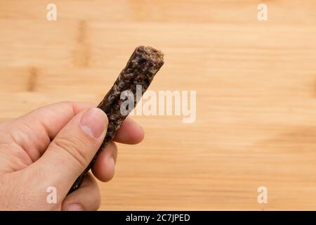 Personne tenant un morceau de biltong avec une surface en bois en arrière-plan Banque D'Images