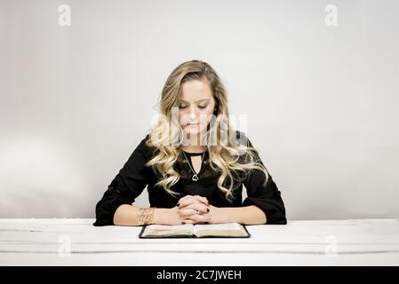 Femme blonde lisant une bible sur la table contre un arrière-plan blanc Banque D'Images