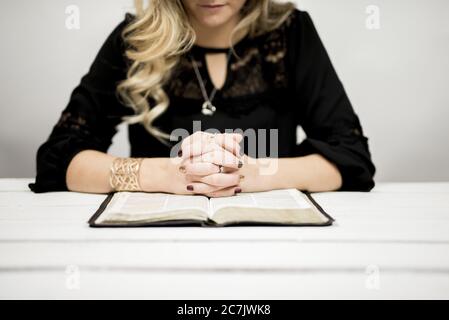 Femme blonde lisant une bible sur la table contre un arrière-plan blanc Banque D'Images