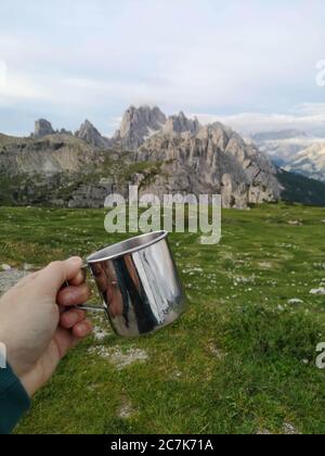 Main tient une tasse de camping, montagnes en arrière-plan Banque D'Images