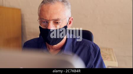 Homme d'affaires travaillant à un bureau portant un masque facial devant un ordinateur. Banque D'Images