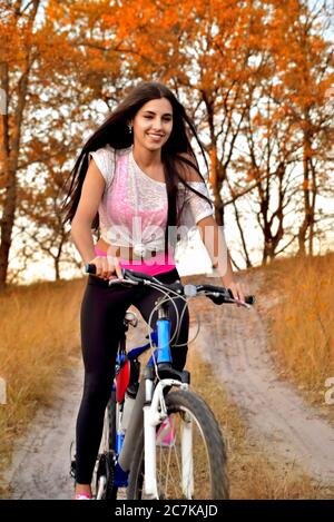 fille à vélo sur une route forestière, souriant de bonne humeur dans les vêtements de sport, coucher de soleil en soirée Banque D'Images