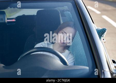 Jeune femme fatiguée endormie sur un oreiller au volant, se reposant après de longues heures de conduite d'une voiture. Fatigue. Privation de sommeil. Banque D'Images