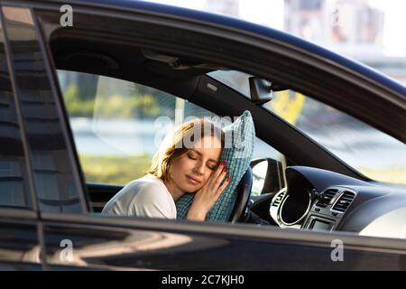Jeune femme fatiguée endormie sur un oreiller au volant, se reposant après de longues heures de conduite d'une voiture. Fatigue. Privation de sommeil. Banque D'Images