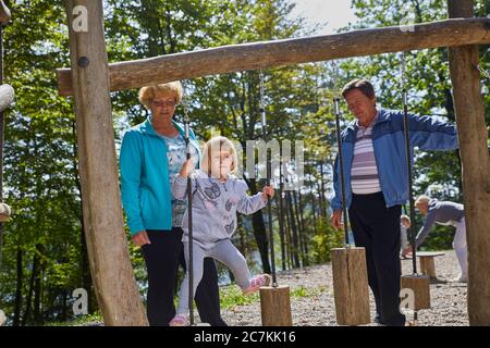 Petite fille jouant sur l'attraction en bois dans l'aire de jeux sous la supervision des parents Banque D'Images