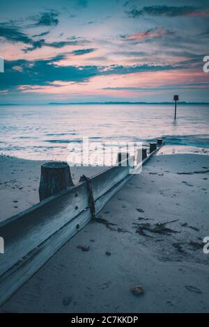 Un lever de soleil calme sur une plage de sable avec une plage de bois Groyne ou marqueur, Hayling Island Beach, Hampshire, Royaume-Uni Banque D'Images