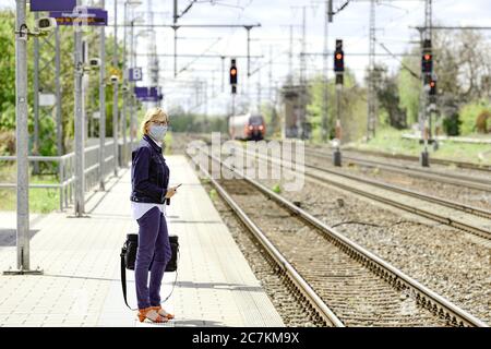 Femme avec un garde-bouche et un porte-documents auto-cousus se tient sur la plate-forme et attend le train Banque D'Images